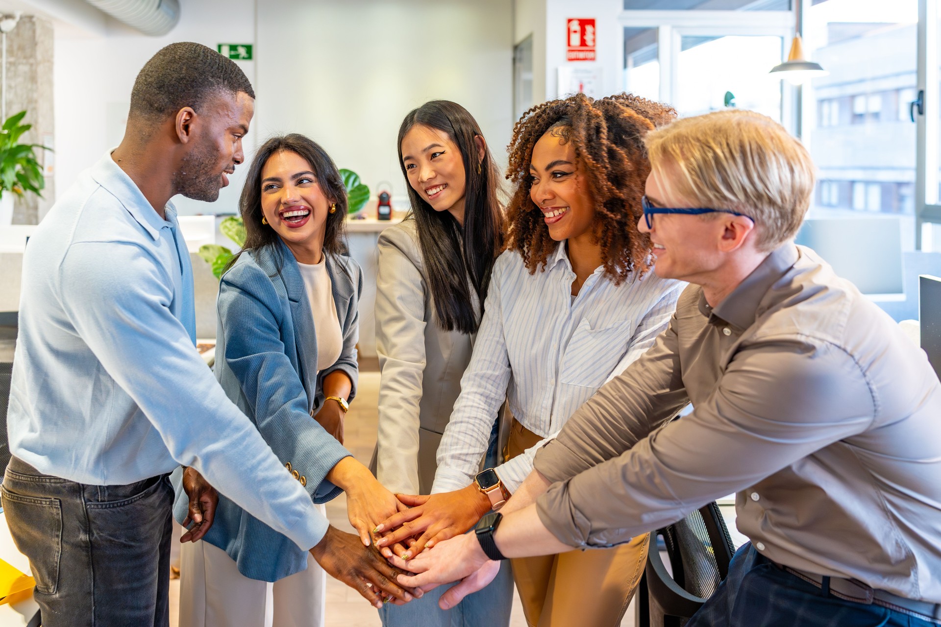 Happy multi-ethnic business team joining hands in coworking office